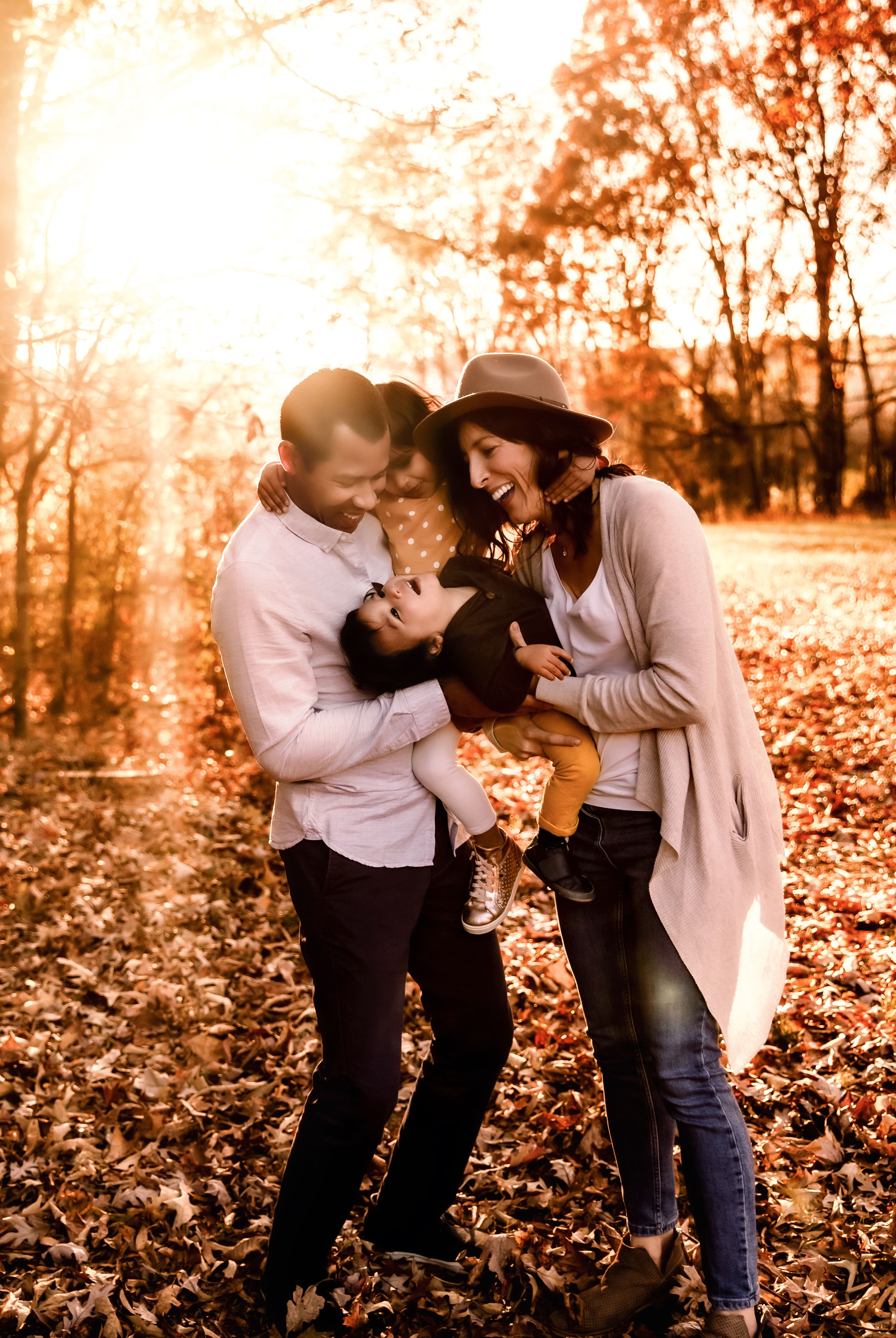 A young couple plays with their child surrounded by fallen autumn leaves.
