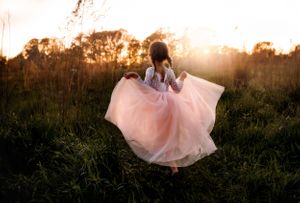 Figure in flowing pink dress twirling in a sunlit field at golden hour.
