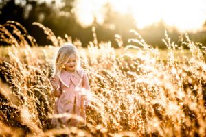 A child in a pink dress playing in golden sunlit wheat fields during sunset.