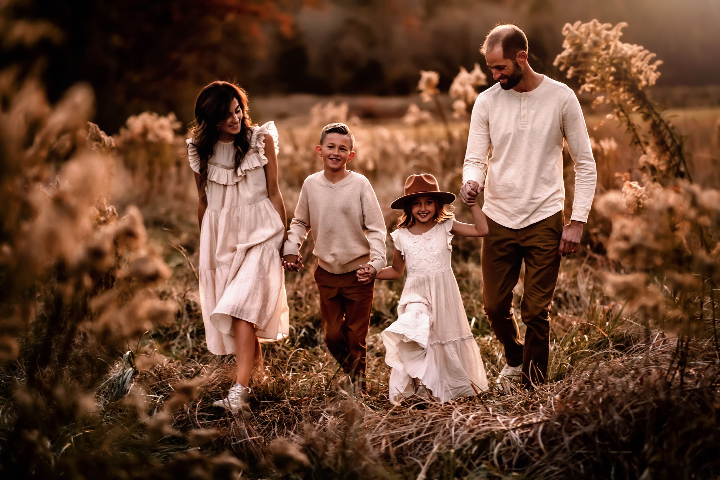 Family walking together through tall grass at golden hour.