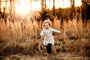 Young child runs joyfully through tall golden grass at sunset.