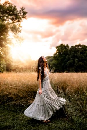 A flowing gray tiered dress twirls gracefully in a golden sunset meadow with trees in the background.