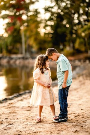 Two young children sharing a sweet moment on sandy beach at sunset.