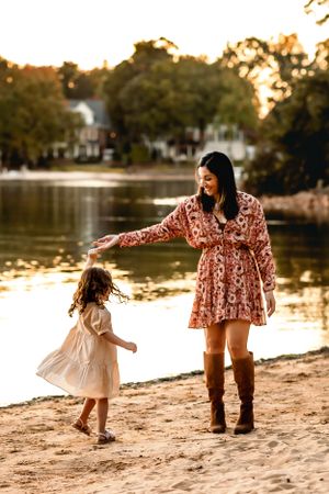 Mother and child dancing together on sandy beach at sunset.