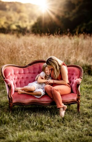People sharing tender moment on vintage pink sofa in outdoor field setting.