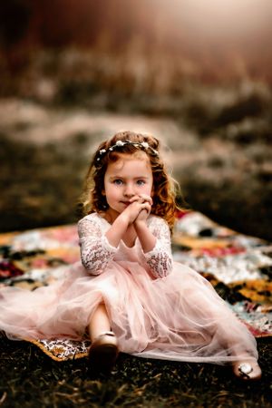 Young child in pink tulle dress with lace sleeves sitting on patterned blanket outdoors.