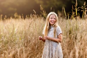 Child in floral dress laughing in golden wheat field at sunset.