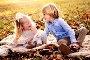 Two children laughing while sitting on blanket with fall leaves.