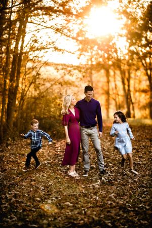 A joyful outdoor photo of a group walking through fallen autumn leaves at sunset in a forest setting.