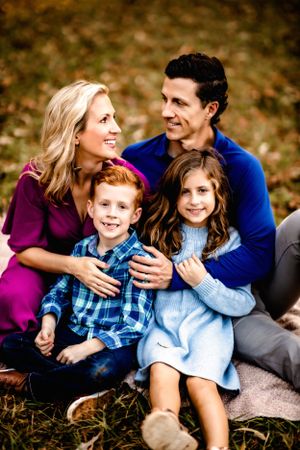 Family portrait with parents and two children sitting together outdoors in autumn.