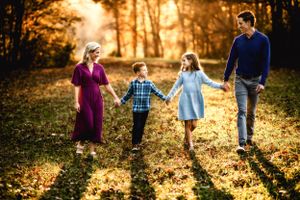 Family walking hand in hand through a sun-drenched autumn forest.