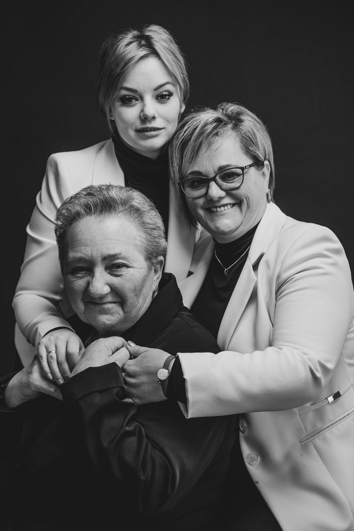 Three-generation family portrait in formal wear against dark background.