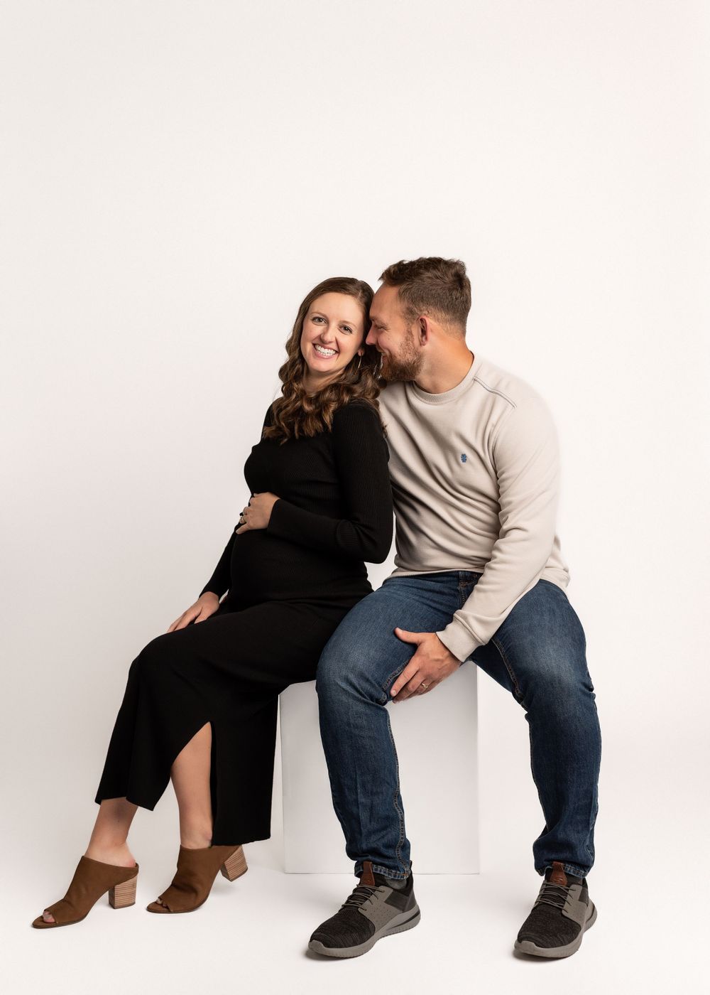 A couple sits together and shares a tender moment against a white background.