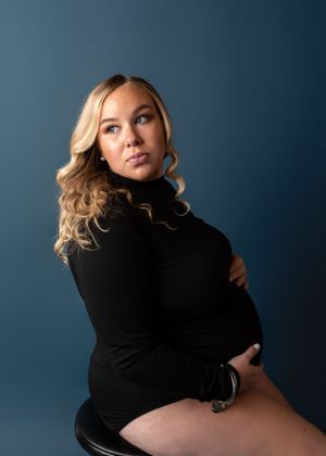 A studio maternity portrait against a deep blue background wearing a black sweater.