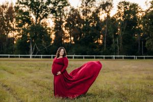 A flowing red dress catches wind as woman poses in field at sunset.