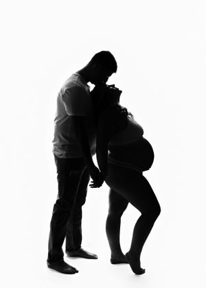 A dramatic black and white silhouette of an expectant couple embracing.