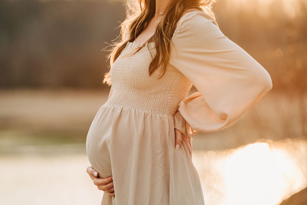 Side profile of pregnant woman in cream dress during golden hour photoshoot.