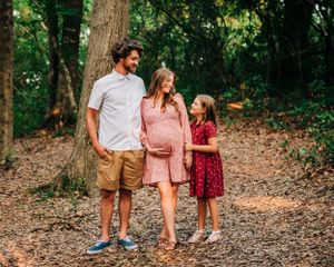 A family shares a tender moment on a wooded path during a maternity photo session.