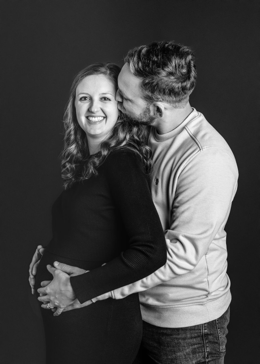 A couple embraces in black and white portrait against dark background.