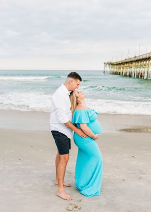 A romantic maternity photo session on the beach with a fishing pier in the background.