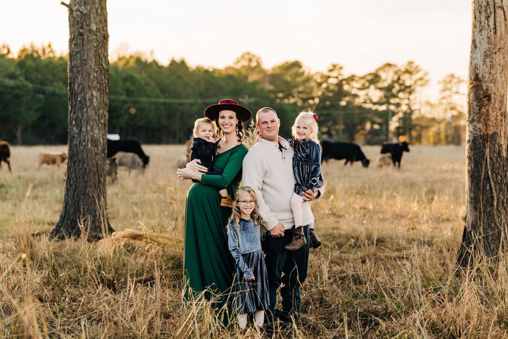 A group stands together in a field with grazing cattle visible in the background at sunset.