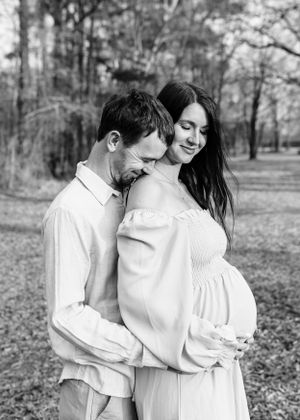 Intimate black and white maternity photo of couple embracing outdoors.