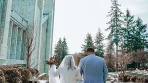 A couple strolls along a pathway surrounded by evergreen trees and modern architecture.