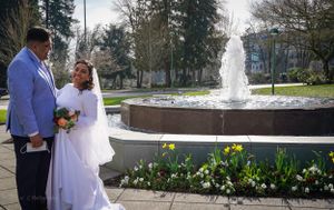 A couple stands beside a fountain surrounded by spring daffodils in a garden setting.