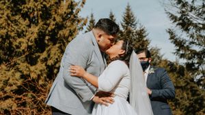 A romantic wedding kiss moment during an outdoor ceremony with pine trees in the background.