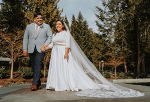 A newlywed couple walking together on a concrete platform with a flowing white wedding dress train.
