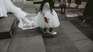 Close-up of a wedding dress train trailing on grey stone steps outdoors.
