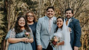 Wedding party group photo with bridesmaids and groomsmen in grey and blue attire against wooded background.