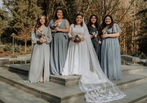 Bridal party in light blue dresses standing with bride in white on outdoor concrete platform.