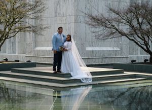 Couple in wedding attire standing on reflective marble steps by modern architecture.