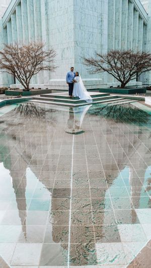 Wedding couple reflected in pool of water against modern marble building architecture.
