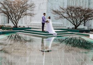 Bride and groom in elegant pose on marble steps with reflection in water below.