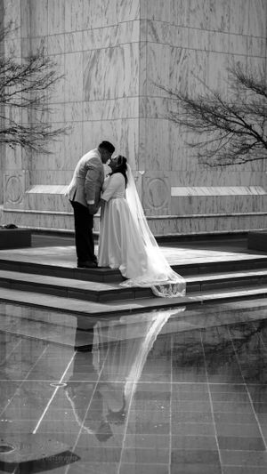 Black and white wedding portrait of couple embracing on marble steps with reflection.