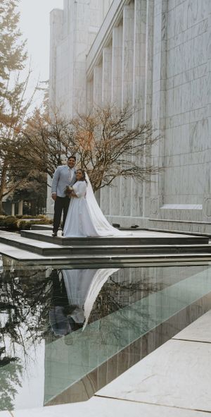 Wedding couple standing on marble steps against white stone building with water reflection.