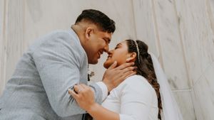 Romantic wedding portrait of couple in tender embrace against white wall background.