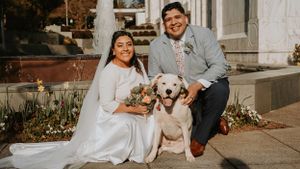 Wedding couple poses with their happy yellow Labrador retriever on stone steps.