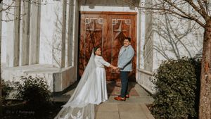 Couple standing in front of ornate wooden doors with cathedral-length veil trailing behind.