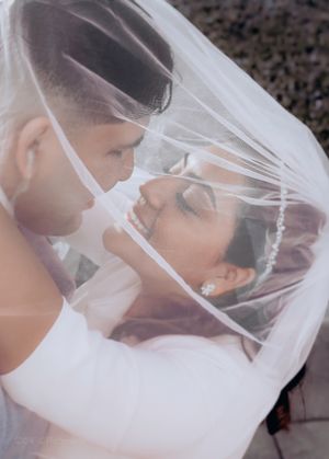 Intimate portrait of newlyweds sharing tender moment under delicate veil.