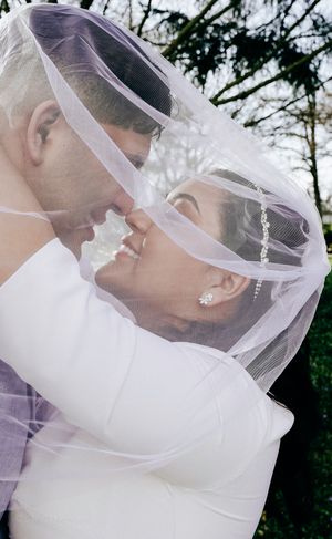 Close-up romantic moment between newlyweds beneath sheer wedding veil.