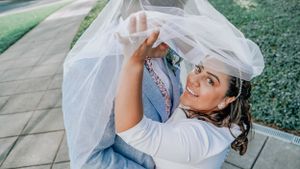 Joyful bride playfully lifts wedding veil while wearing white dress.