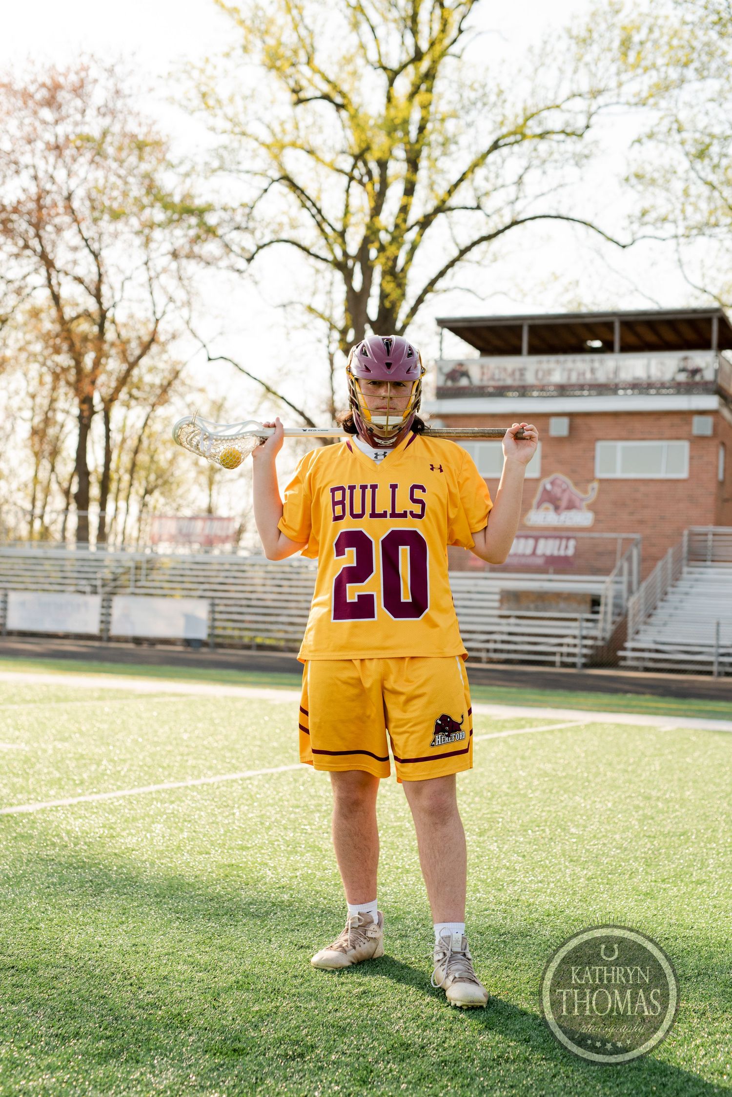 Player wearing yellow Bulls jersey number 20 poses with lacrosse stick on athletic field.