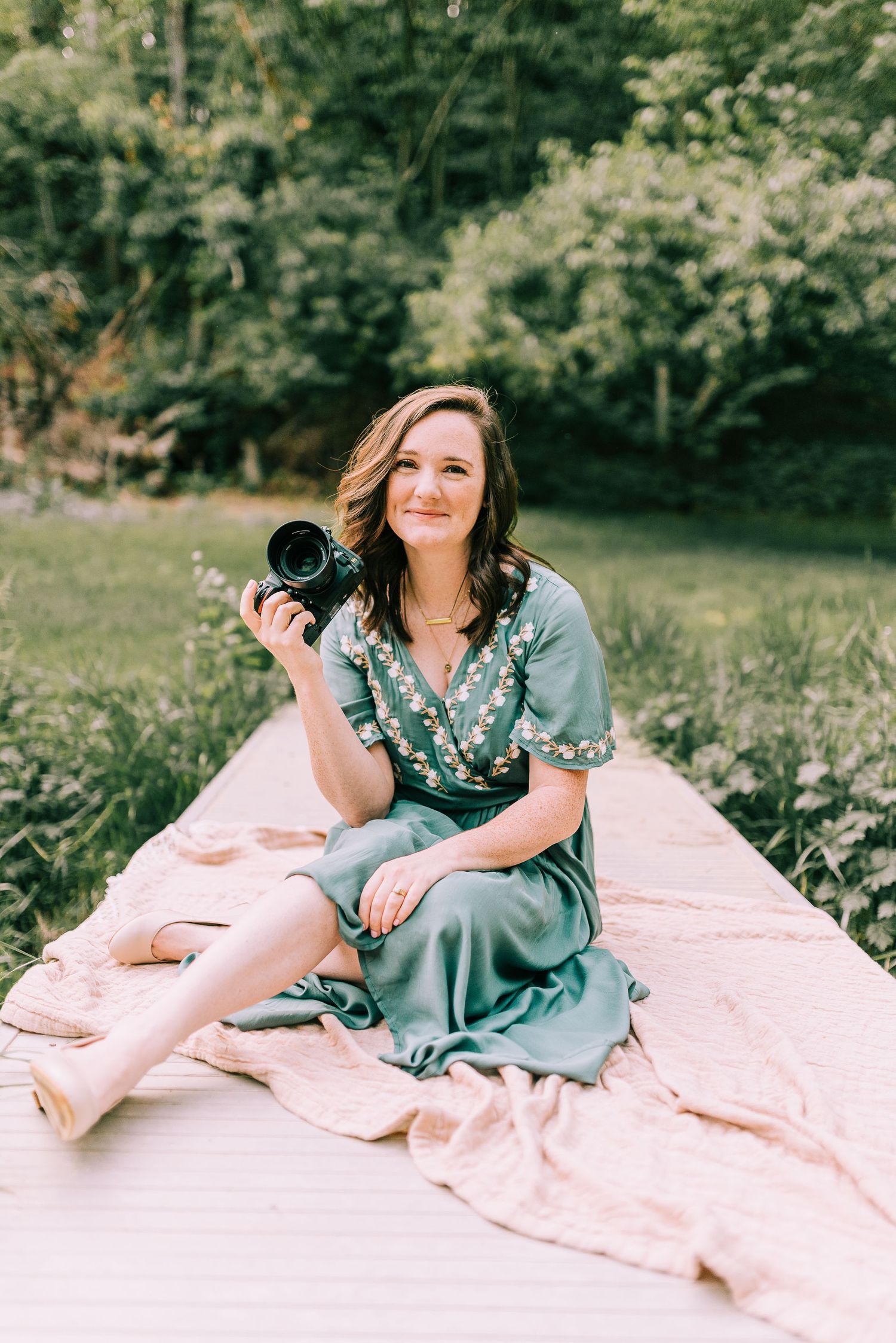 Photographer sitting on a small bridge in a green dress, holding her camera