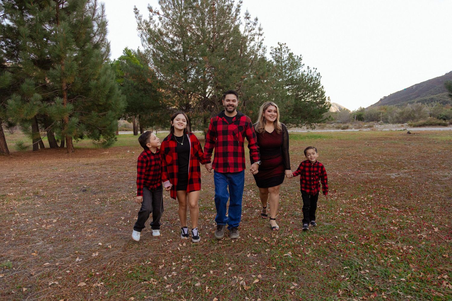 Family in matching red plaid flannel shirts walking together on autumn grounds.