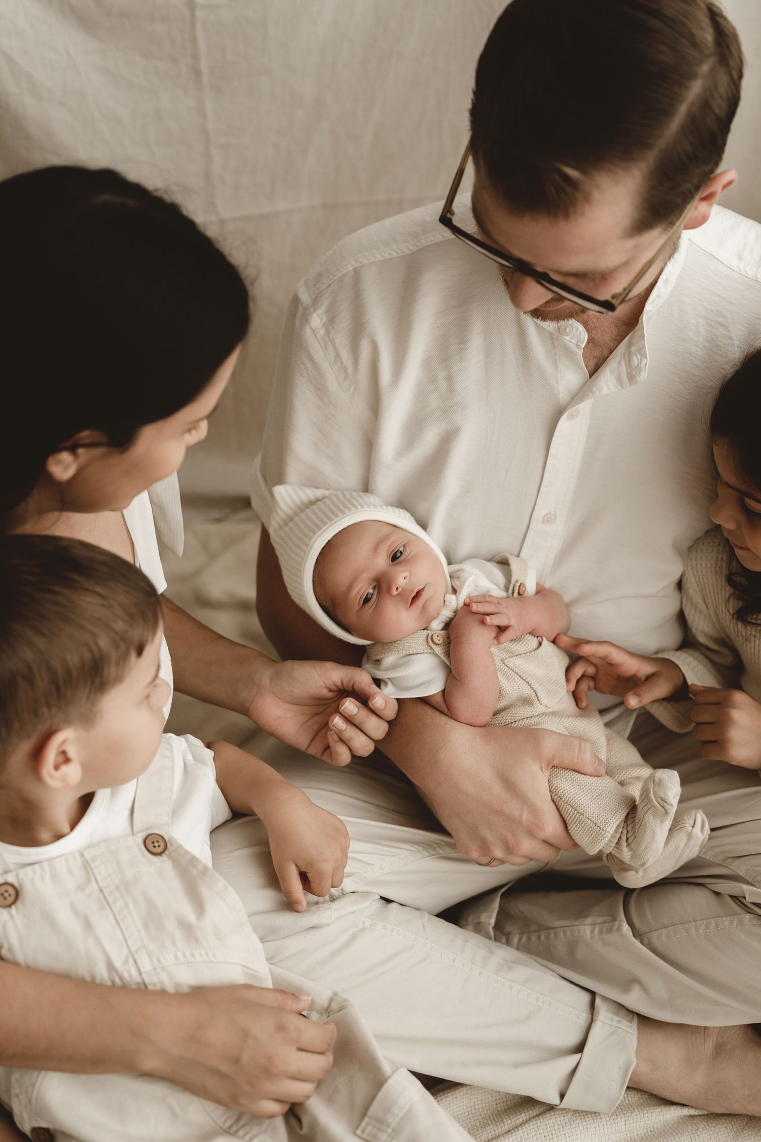 Family gathered around newborn baby wearing white bonnet.