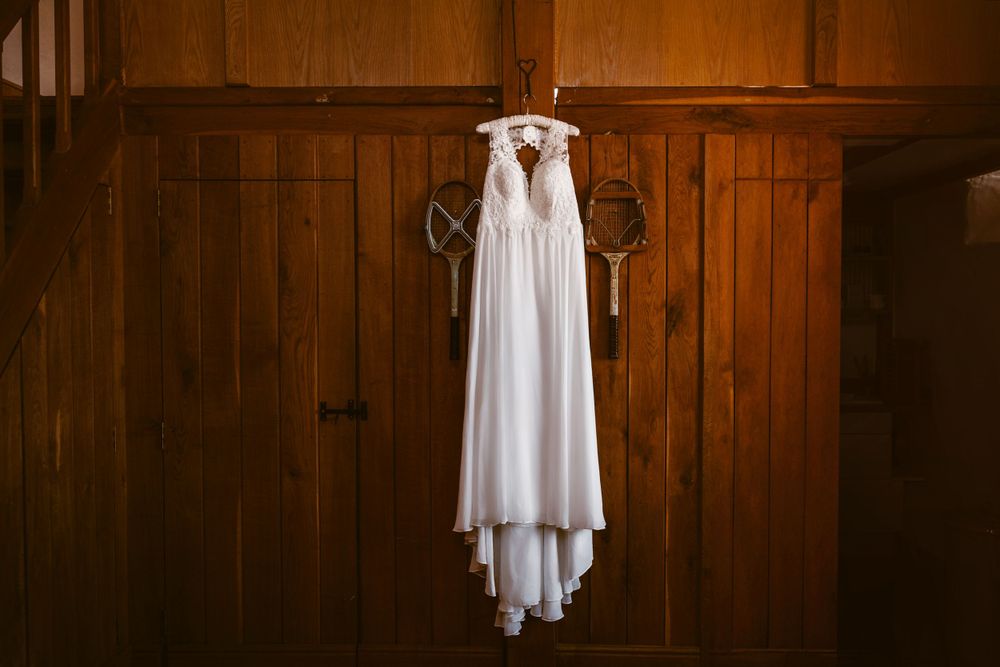 Elegant white wedding dress hanging against wooden paneled walls in warm lighting at Merriscourt.