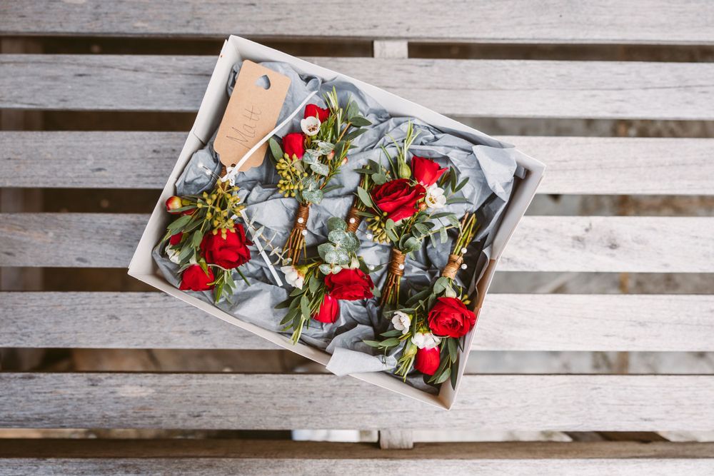 Box of red roses and greenery arranged for wedding decoration on wooden surface.